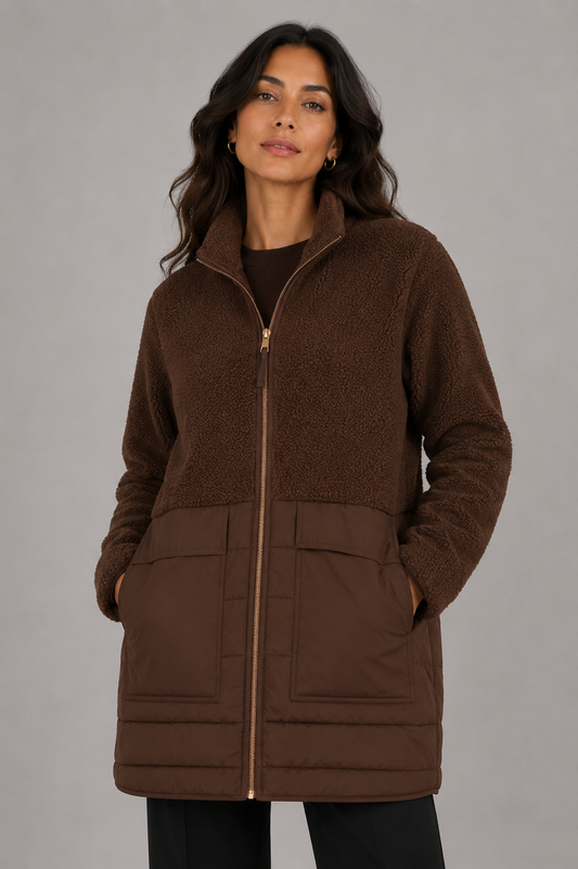 A woman wearing a brown fleece zip-up jacket with a quilted lower panel and front pockets, photographed against a plain gray studio background.
