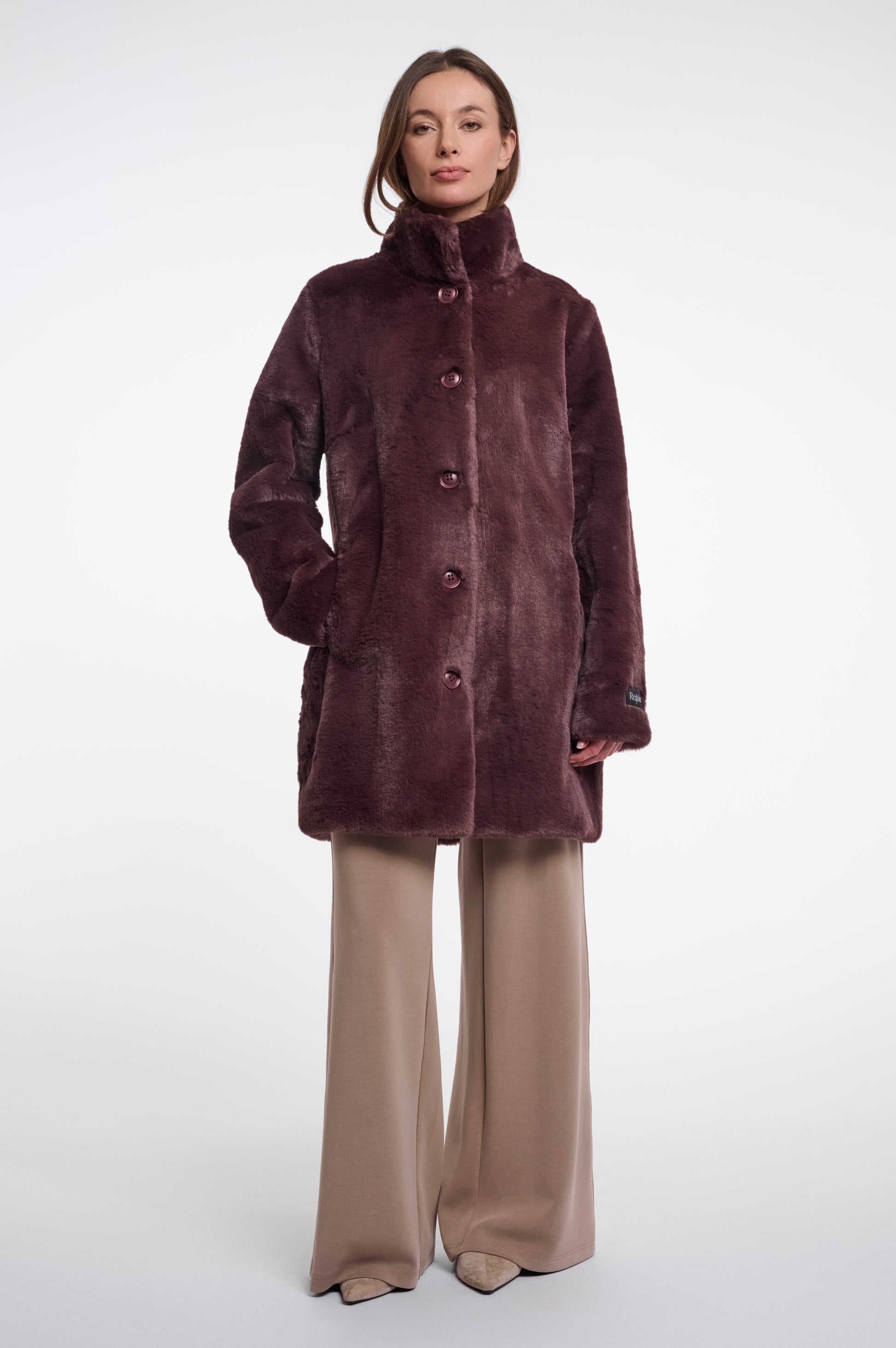 Woman wearing a brown coat and beige pants on a white background